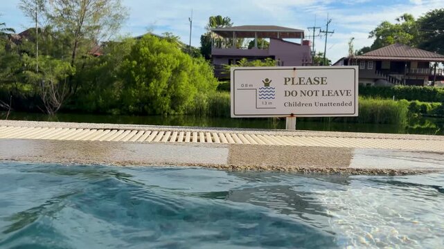 A safety warning sign standing by the edge of a swimming pool, instructing people not to leave children unattended.
