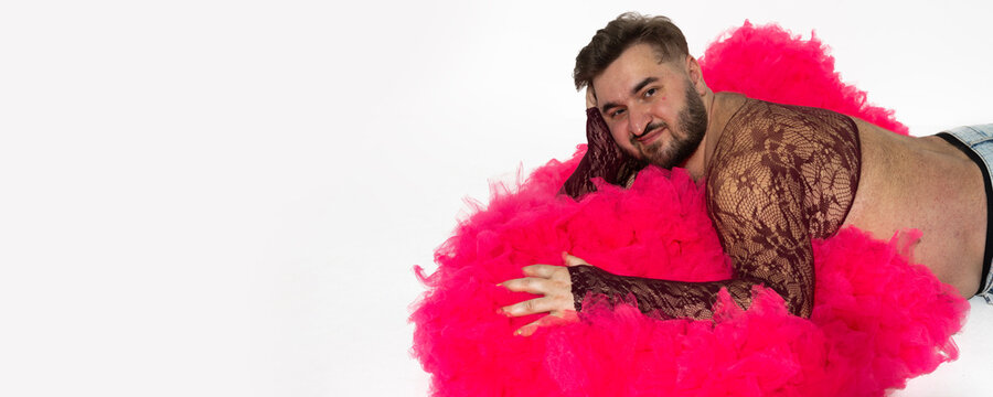 Photo banner. Mature white man with beard, mesh through tank top, big belly, blue jeans, magenta tulle fur coat, lies on floor, looks at camera on white. LGBT pride month, beauty, fashion. Copy space