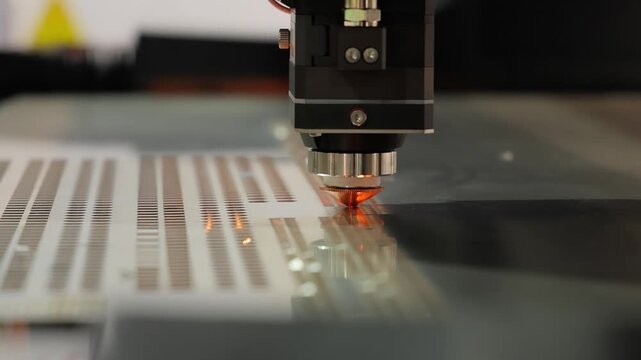 Precision laser cutter etches intricate patterns onto metal sheet in industrial manufacturing setting.