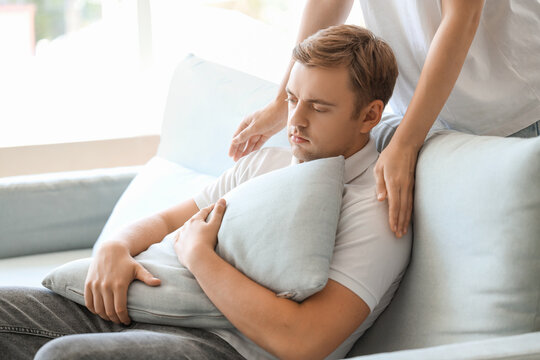 Woman supporting man with suicidal thoughts and pillow on sofa at home