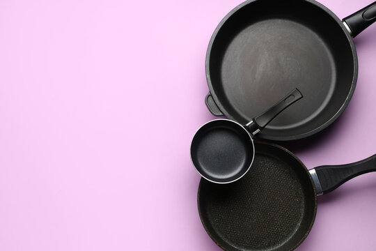 Assortment of black non-stick frying pans and saucepans for home cooking and kitchen utensils on a pink background, the clean