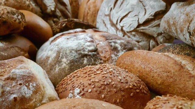 Freshly baked artisan bread assortment featuring various rustic sourdough loaves and crispy buns in a bakery display.