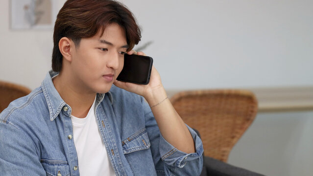 Serious Young Asian Man Talking on Smartphone in Denim Shirt