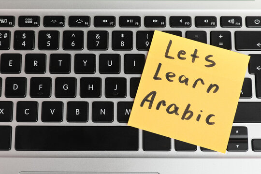 Online arabic language learning with yellow sticky note on laptop keyboard for digital education, the note displays "lets learn arabic" in black handwritten text, digital education and remote
