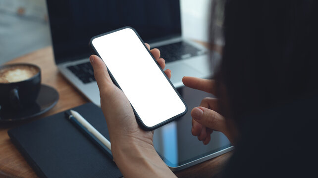 Mockup, Woman using mobile phone with blank white screen while online working on laptop at coffee shop. Business woman using smartphone, mockup for mobile app marketing, closeup