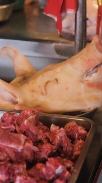 Vertical video. Market butcher counter in Thailand displaying various raw meat cuts alongside a whole pig head as part of the fresh produce on offer. Traditional market concept