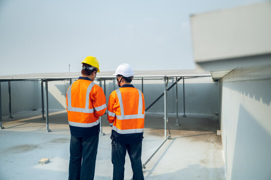 Young technician and Engineer inspect solar panels on steel framework on building rooftop. Installation planning, Maintenance and inspection renewable energy, Energy-efficient buildings project.