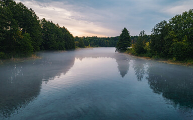 Fototapeta premium Serene morning mist covers peaceful lake surrounded by green forest