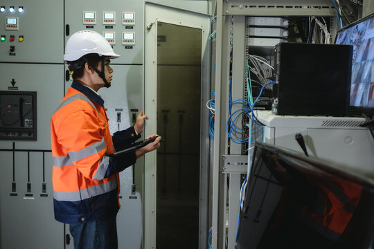 Asian young IT engineer in uniform using tablet and open to server rack cabinet, Systems engineer in safety gear examines server equipment, Configuring network switches computer system indoor