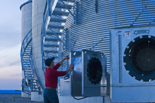 a man turns on an aeration fan on a  grain storage bins in the evening