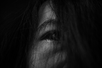 Fototapeta premium Close Up of Eye Hidden Behind Hair in Darkness Showing Fear and Anxiety