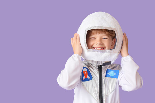 Happy young boy in astronaut costume with helmet smiling, space exploration and childhood dreams concept, the child wears a white and silver suit with rocket and planet patches