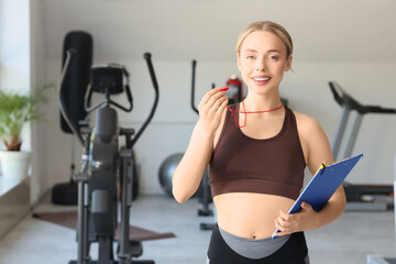 Fototapeta premium Smiling female personal trainer holding whistle and clipboard in modern gym setting, fitness coaching and wellness lifestyle