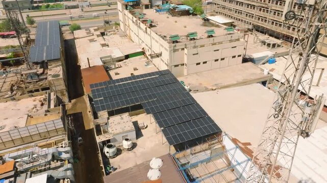 Large solar panel installation on a factory roof within a dense manufacturing district of Karachi. Aerial orbit looking down.