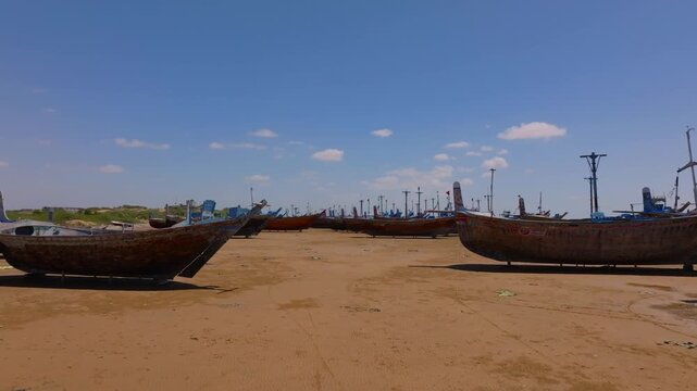 Large traditional wooden fishing vessels resting on the sunny sands of Damb Beach during low tide. Forward ascending aerial tilting down.