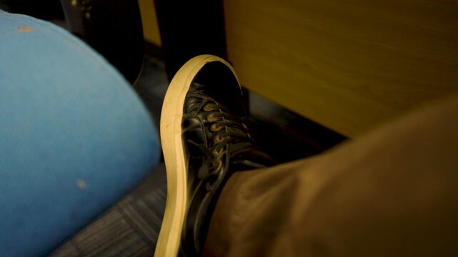 Male student's nervous leg and foot pacing left and right in a university classroom setting in Karachi. Static close up focusing on leg and foot.