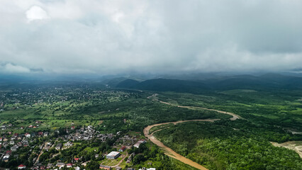 Overcast sky looms above a rural town with gardens pastures and winding roads. The aerial view reveals a broad valley system shaped by rivers fields and gentle hills. © Oleh