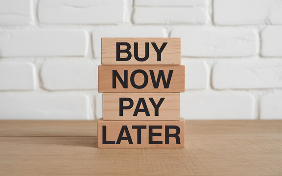 A stack of wooden blocks with buy now pay later text on a white brick wall background