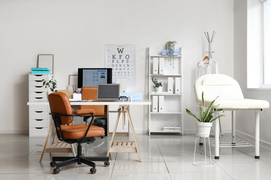 Modern doctors office interior with examination couch, desk, laptop, and eye chart for medical consultation