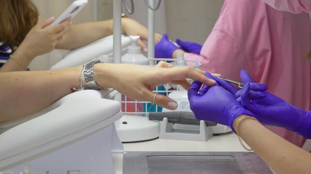 The technician wears purple protective gloves and carefully cleans the fingernail and cuticle area with a wooden manicure stick.