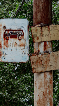Old weathered transport schedule signs mounted on a rusty column against green foliage