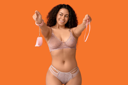 Smiling young woman in lingerie holding pink handcuffs and ribbon, playful adult relationship