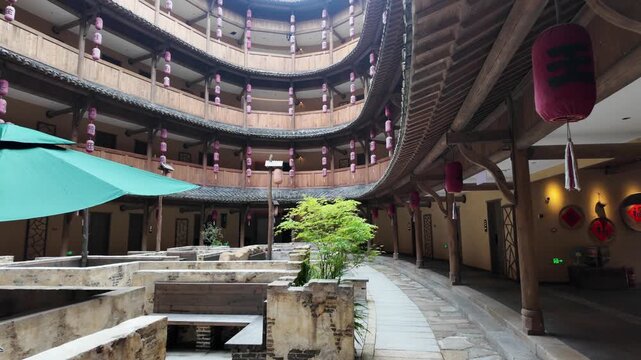 Wangxian Valley, China, 04 April 2026 ? Interior courtyard of a circular Hakka Tulou building with wooden balconies, pink lanterns, stone ruins, and lush spring greenery.