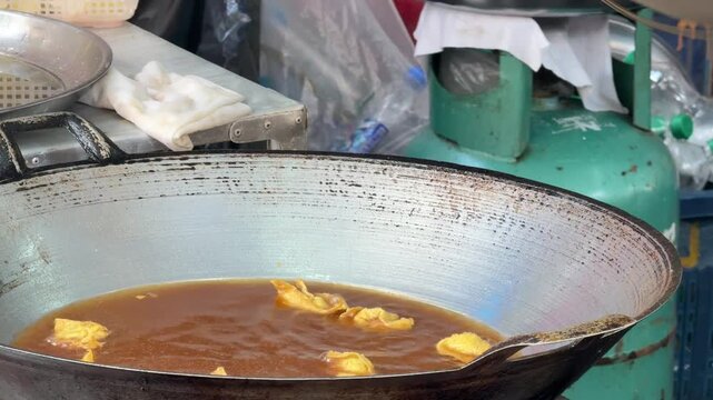 4K footage of deep-fried vegetarian tofu being scooped out of boiling hot oil and shaken on a mesh strainer to drain excess oil.
