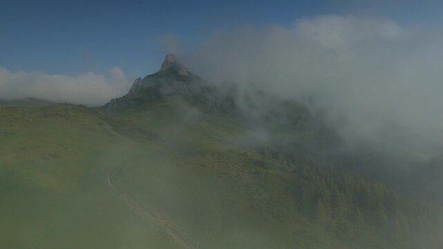 Spectacular early morning in Ciucas Mountains with Tigaile Mari peak breaking through fast-moving clouds, high altitude aerial forward flight, fly through, graded