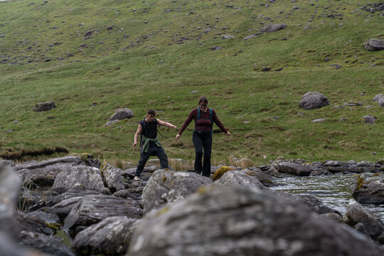 Couple hiking and balancing on rocks crossing stream