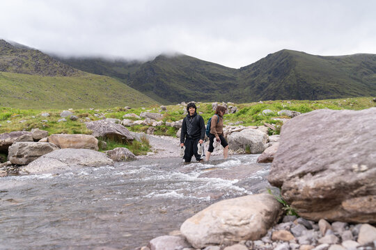 Hikers crossing mountain stream on a cloudy day