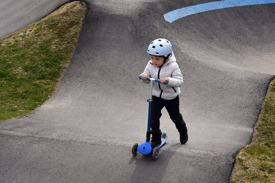 Young boy riding a blue scooter at a skatepark wearing a helmet and
