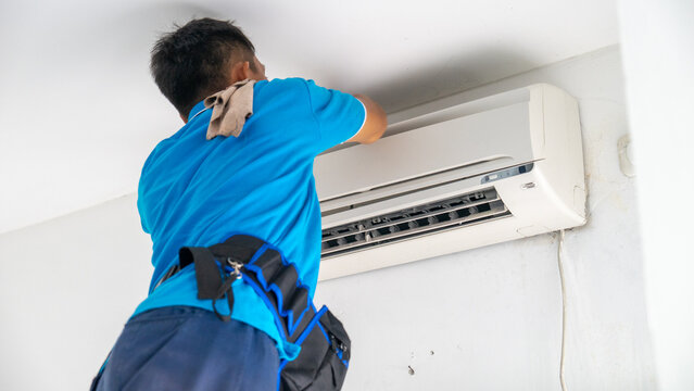 Professional Technician in Blue Uniform Repairing and Servicing a Wall-Mounted Air Conditioner Unit Indoors