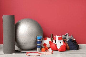 Obraz premium Different sports equipment and bag with shoes on floor near red wall