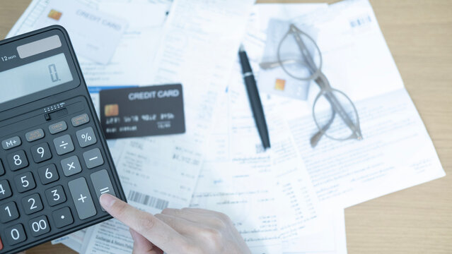 Hand pressing a calculator while reviewing monthly bills, receipts and credit card expenses for household budget planning and debt management.