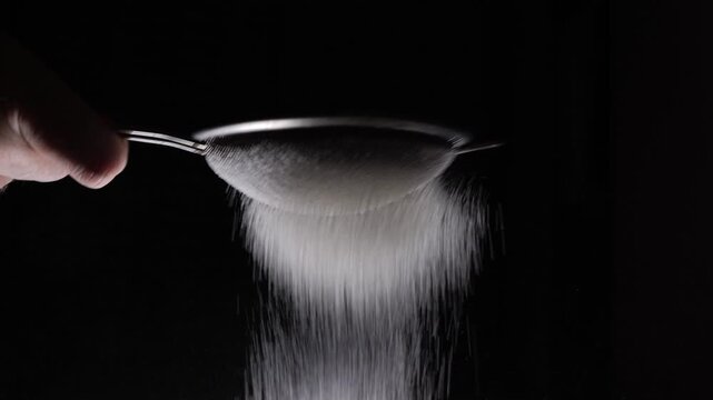 Sifting flour for baking and desserts on a black background, working with flour