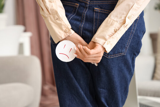Young woman with hemorrhoids and sad smile at home, back view