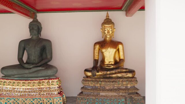 A trucking shot of golden and stone Buddha statues standing in a row, representing Buddhism and spiritual beliefs, decorating the historic grounds of Wat Pho temple in Bangkok, Thailand