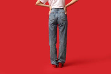 Naklejka premium Beautiful young Asian woman in stylish jeans on red background, back view