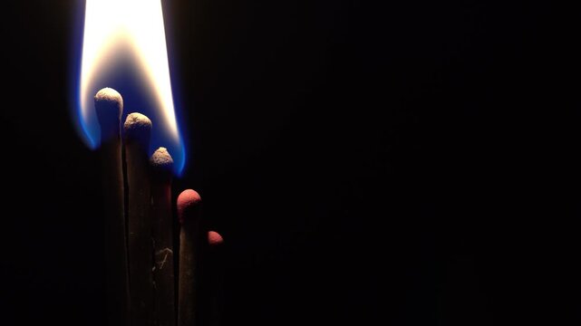 Matches are lit on a black background, close-up view, fire