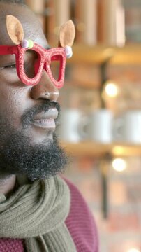 Vertical video: Turning man in sweater seeing camera, shifting, smiling in cafe with red glasses
