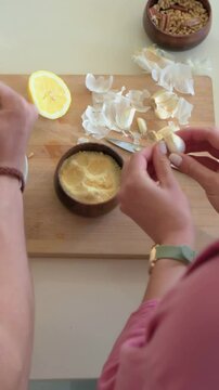 Vertical video: Peeling woman pink top, apron chopping garlic with knife on wood board, copy space