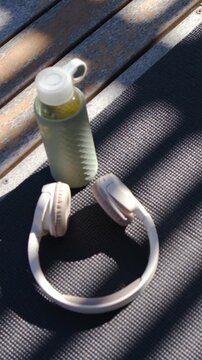 Vertical video: Tilting handheld camera revealing bottle and beige headset details on bench