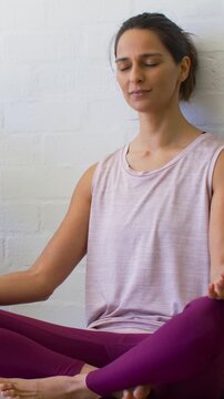 Vertical video: Settling woman meditating for calm at home, wearing tank and leggings by brick wall