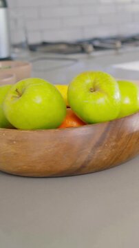 Vertical video: Panning camera revealing wooden fruit bowl on countertop with apples bananas knife