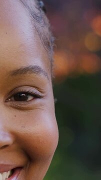Vertical video: Smiling teen moving into frame in park, revealing gold hoop earring and glossy lips