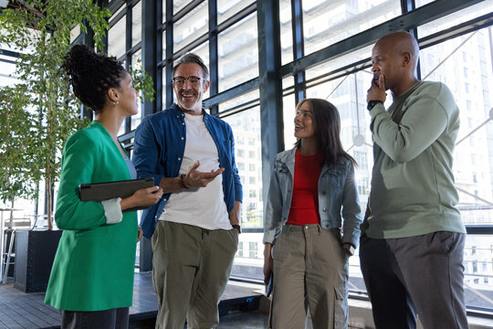 Diverse coworkers standing on deck atrium holding tablet and phone near plant, wearing work clothes