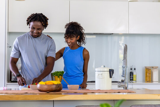 African American couple chopping vegetables on cutting board at wooden island, fruit bowl visible