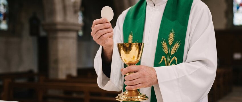 Catholic priest holding the holy eucharist host and golden chalice during mass