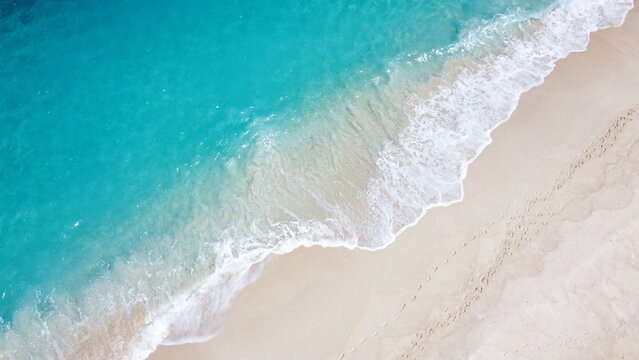 Aerial birdseye view of remote exotic tropical island with white frothy waves, sandy beach, and turquoise ocean water in paradise